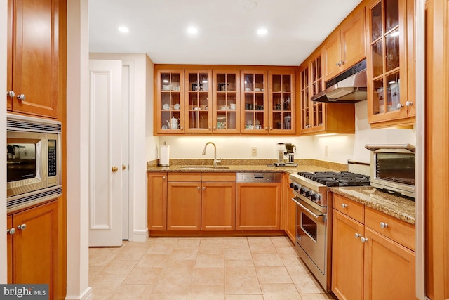 1155 23rd St NW Unit 2E, Washington, DC 20037 - kitchen featuring under cabinet range hood, stainless steel appliances, a sink, glass insert cabinets, and light stone counters