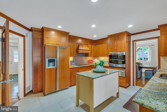 kitchen with paneled built in fridge, decorative backsplash, crown molding, premium range hood, and light stone countertops