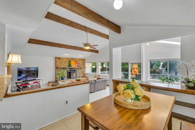 dining space with ceiling fan, light tile patterned flooring, and a stone fireplace