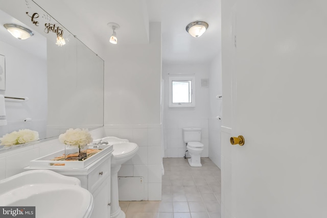 bathroom featuring tile patterned floors, tile walls, toilet, and a sink