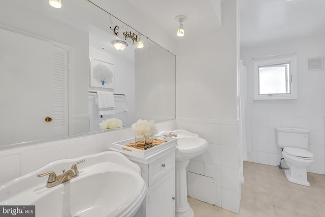 bathroom with tile patterned floors, a sink, toilet, tile walls, and wainscoting