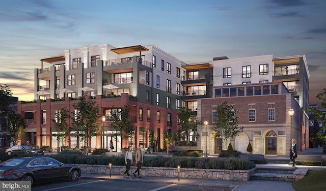 property at dusk with a view of apartment building / complex and uncovered parking
