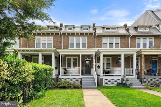 townhome / multi-family property featuring brick siding, a front yard, covered porch, and mansard roof
