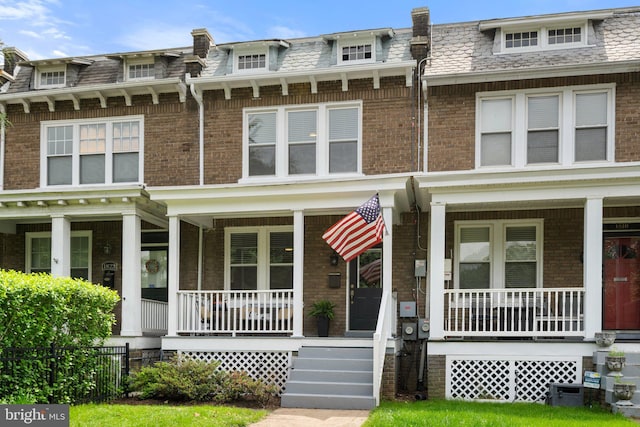 view of front of property with a porch, mansard roof, and brick siding