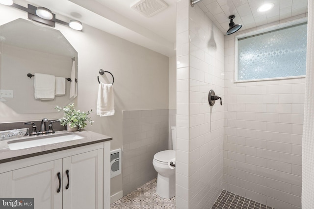 bathroom with tiled shower, toilet, tile walls, vanity, and a wainscoted wall