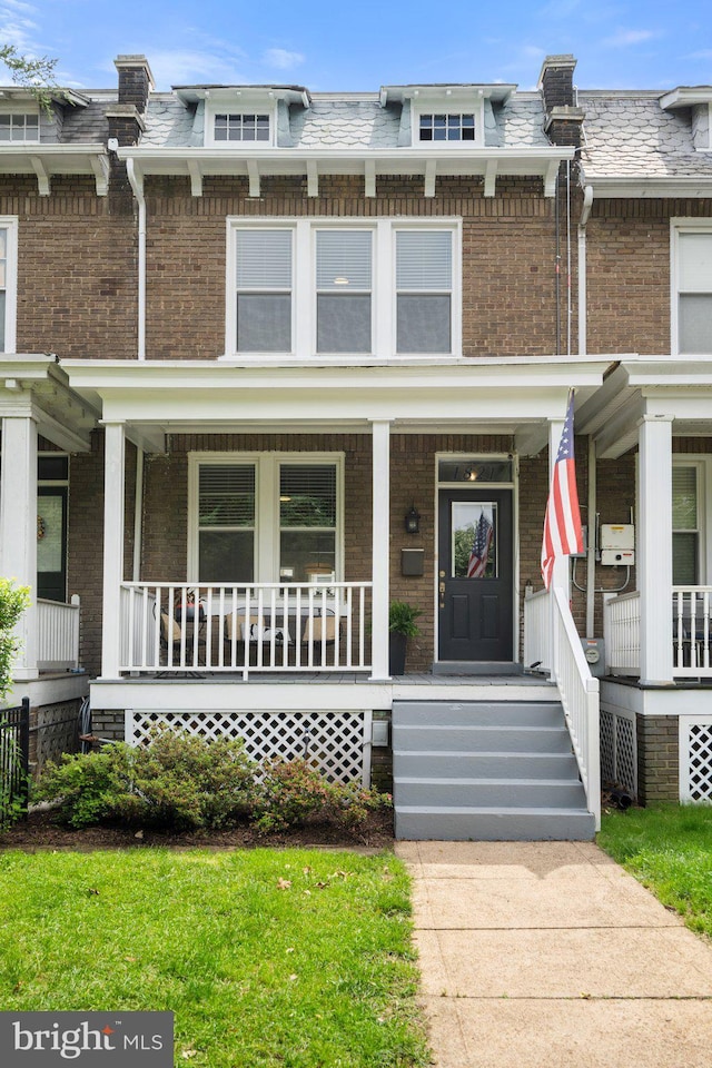 multi unit property with brick siding, covered porch, and mansard roof