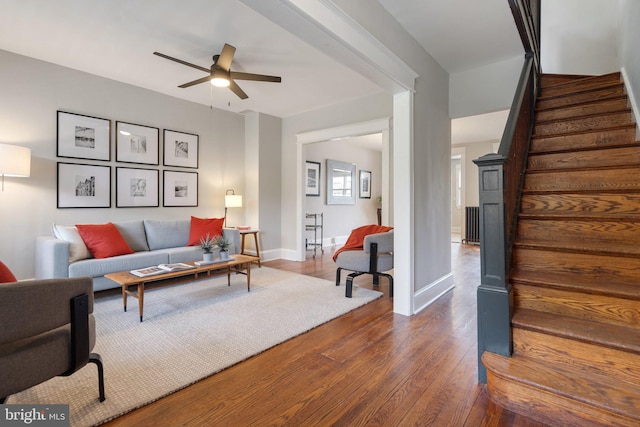 living area with stairs, a ceiling fan, dark wood finished floors, and baseboards