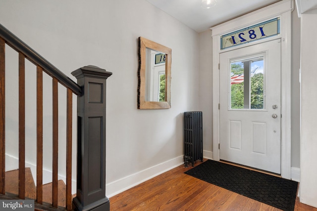foyer entrance with stairway, wood finished floors, baseboards, and radiator