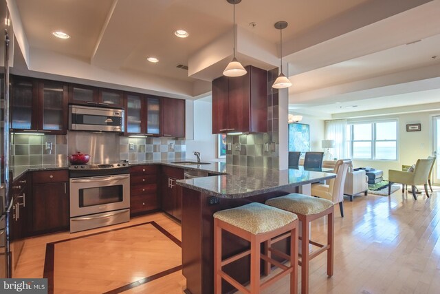 kitchen featuring stainless steel appliances, a sink, open floor plan, a peninsula, and a breakfast bar area
