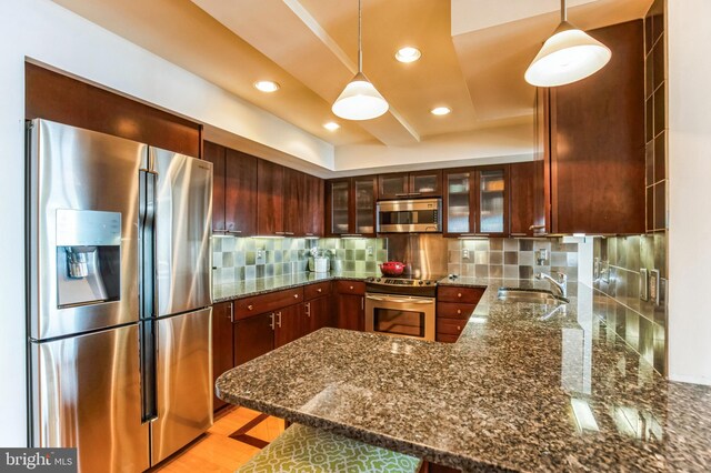 kitchen with appliances with stainless steel finishes, a sink, a peninsula, dark stone counters, and hanging light fixtures