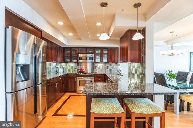 kitchen featuring appliances with stainless steel finishes, a sink, a peninsula, backsplash, and glass insert cabinets