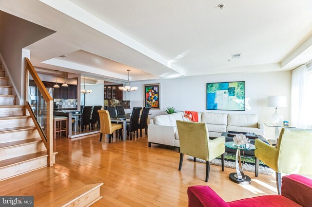 living room with a tray ceiling, stairway, a chandelier, and hardwood / wood-style flooring