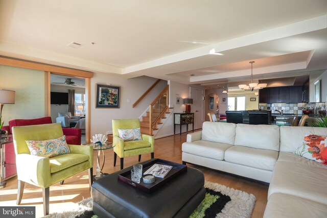 living area with a tray ceiling, stairs, wood finished floors, and a chandelier