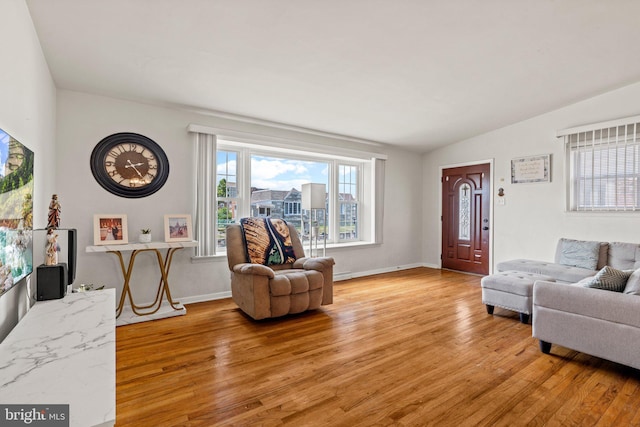 living room featuring light wood-style floors, vaulted ceiling, and baseboards
