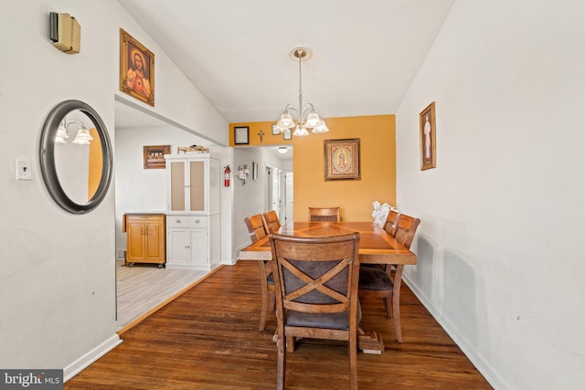 dining area featuring a chandelier, baseboards, wood finished floors, and vaulted ceiling