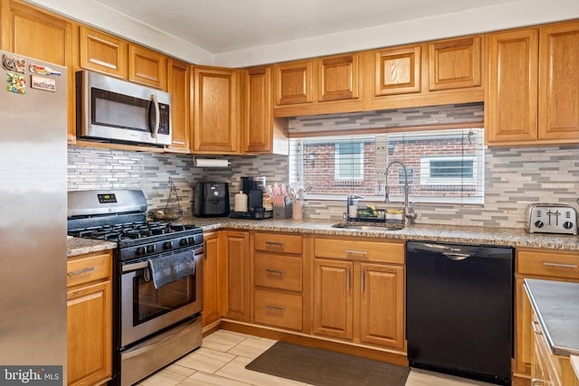 kitchen with stainless steel appliances, a sink, backsplash, brown cabinets, and light tile patterned flooring
