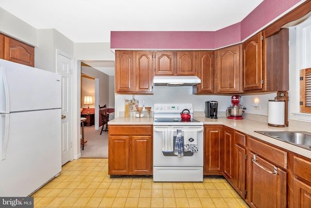 kitchen with white appliances, under cabinet range hood, light countertops, a sink, and brown cabinetry