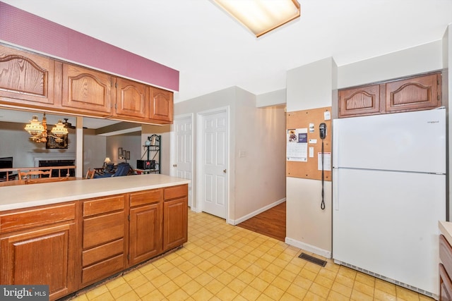 kitchen with freestanding refrigerator, light countertops, brown cabinetry, baseboards, and a chandelier