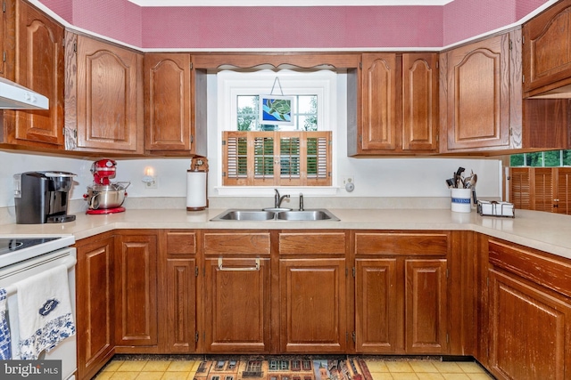 kitchen with a sink, electric stove, light countertops, light tile patterned floors, and brown cabinetry