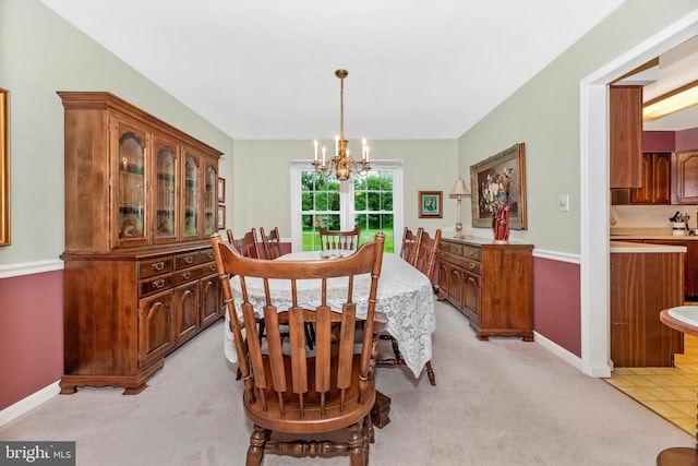 dining room with a chandelier, light colored carpet, and baseboards
