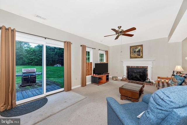 carpeted living area with a fireplace, a ceiling fan, healthy amount of natural light, and baseboards
