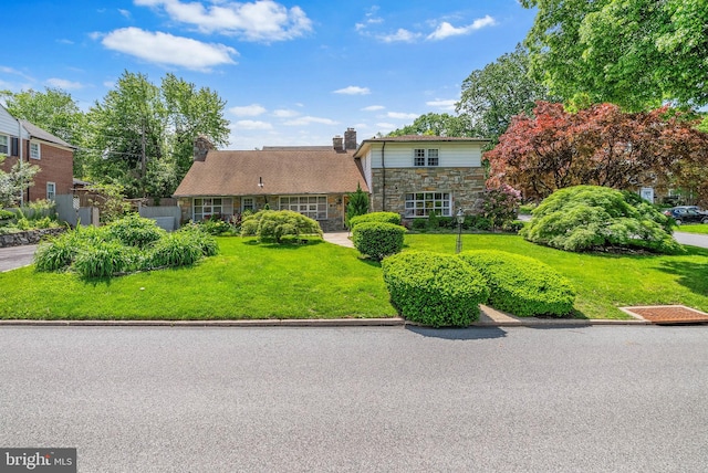 view of front of house with stone siding, a front lawn, and a chimney