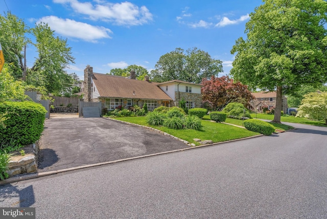 view of front of property with asphalt driveway, stone siding, a garage, and a chimney