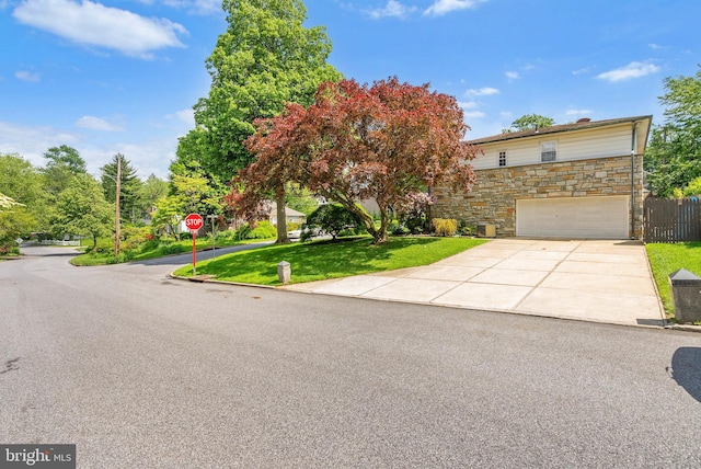 view of property hidden behind natural elements with stone siding, an attached garage, and driveway
