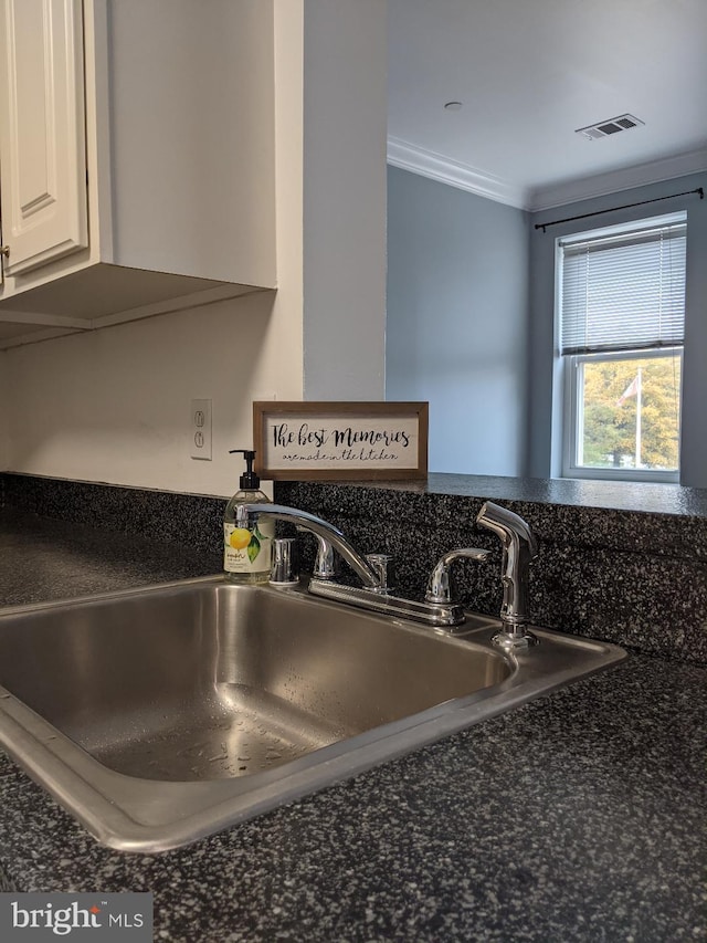 kitchen view of a sink, dark countertops, crown molding, and white cabinetry
