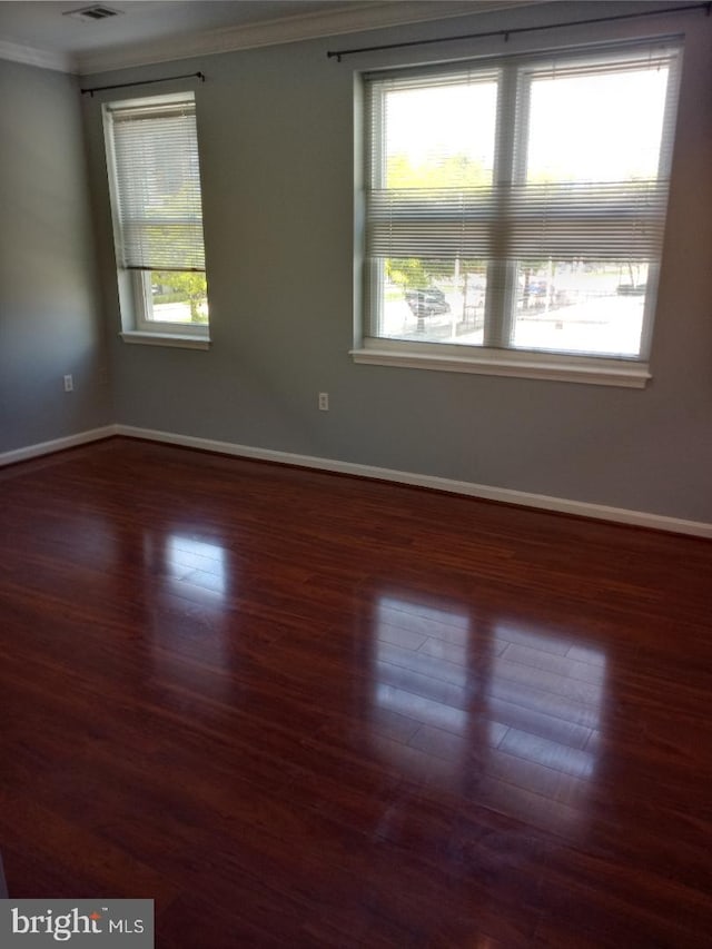 empty room featuring crown molding, baseboards, and wood finished floors