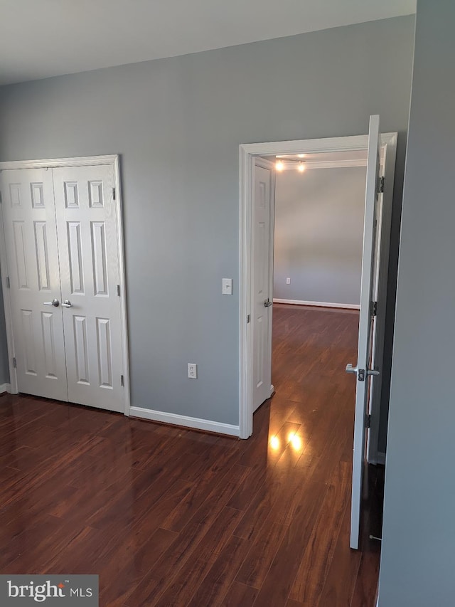 unfurnished bedroom with dark wood-type flooring, baseboards, and a closet