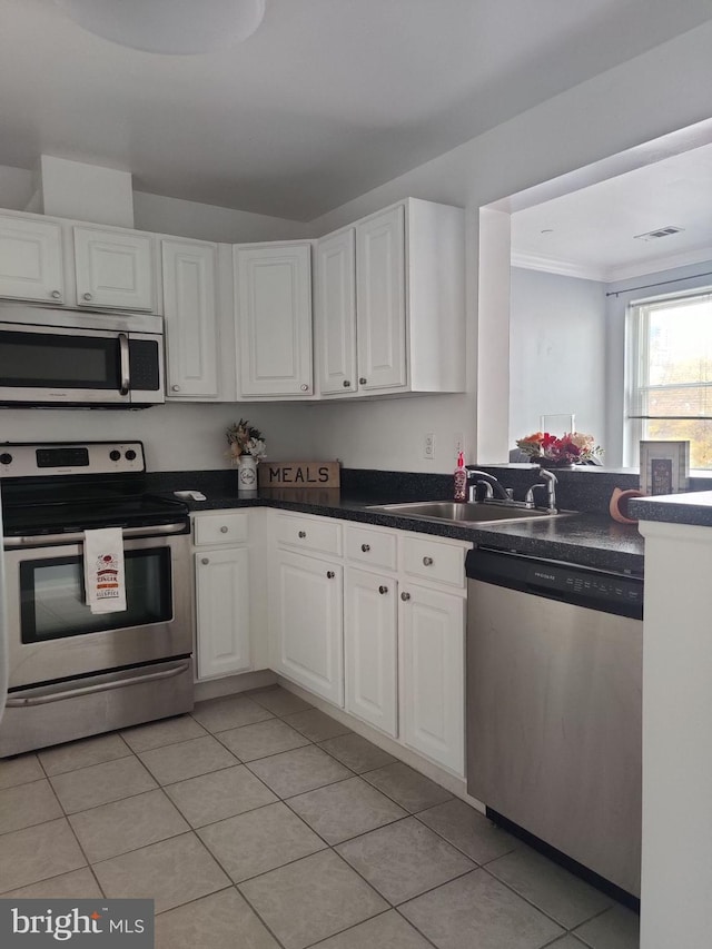 kitchen featuring stainless steel appliances, a sink, light tile patterned flooring, white cabinets, and ornamental molding