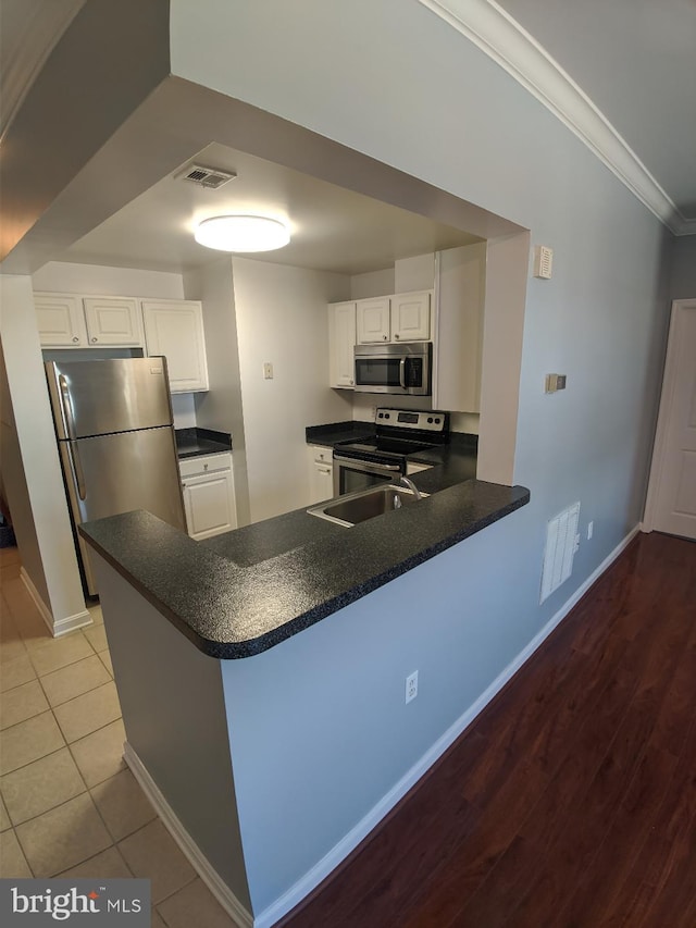 kitchen featuring appliances with stainless steel finishes, crown molding, dark countertops, a peninsula, and white cabinetry