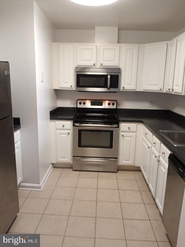 kitchen with stainless steel appliances, white cabinets, light tile patterned floors, and baseboards