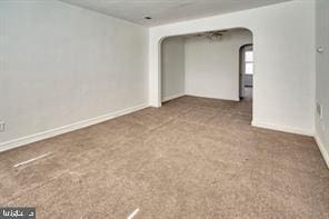 empty room featuring arched walkways, carpet floors, and baseboards