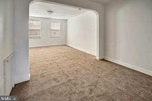 spare room featuring carpet flooring, arched walkways, and baseboards