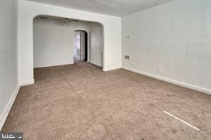 carpeted empty room featuring arched walkways and baseboards