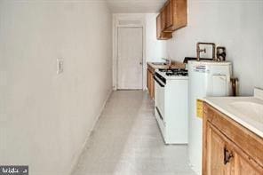 kitchen with white gas range oven, light countertops, brown cabinetry, and baseboards
