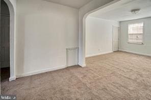 carpeted spare room featuring arched walkways and baseboards