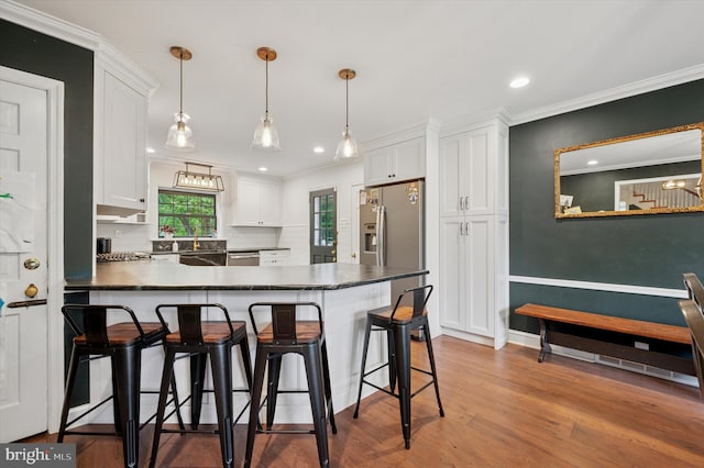 kitchen with dark countertops, white cabinets, a kitchen bar, a peninsula, and wood finished floors