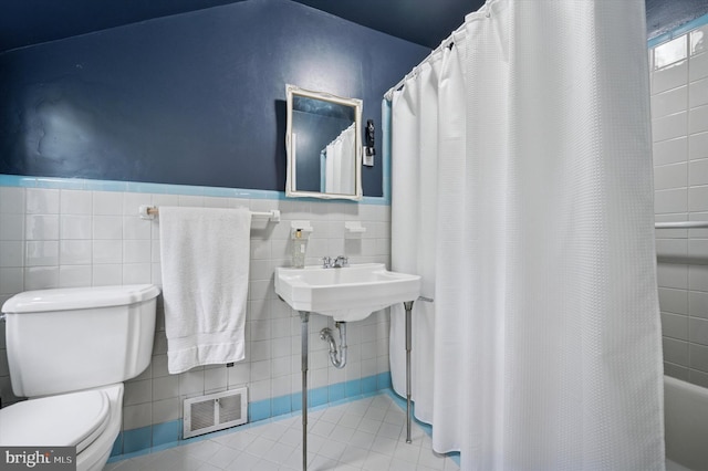 full bathroom with toilet, tile patterned flooring, tile walls, a shower with shower curtain, and wainscoting