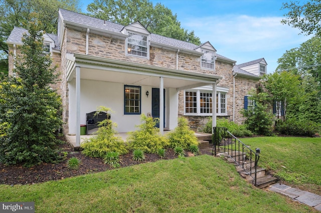 traditional-style home with stone siding, a front yard, stucco siding, and a porch