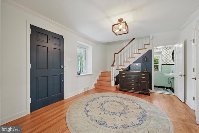 foyer with stairs, light wood-type flooring, ornamental molding, and baseboards
