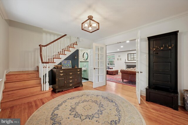 foyer entrance featuring stairs, ornamental molding, light wood finished floors, a chandelier, and french doors