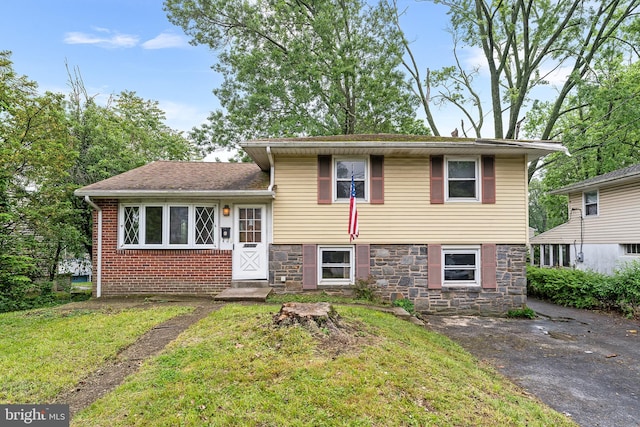 split level home featuring stone siding and a front lawn