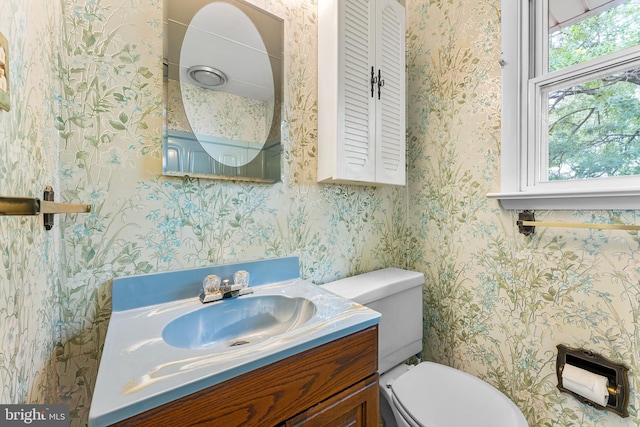 half bath with vanity, toilet, and wallpapered walls