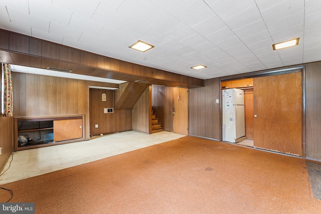 finished below grade area with freestanding refrigerator, carpet floors, stairway, and wooden walls