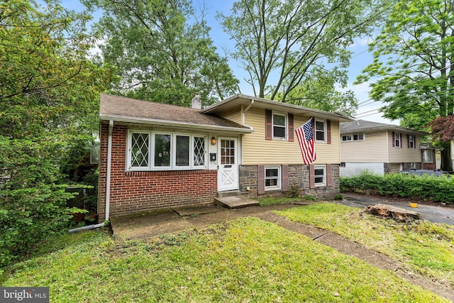 tri-level home featuring a front lawn, stone siding, a chimney, and brick siding