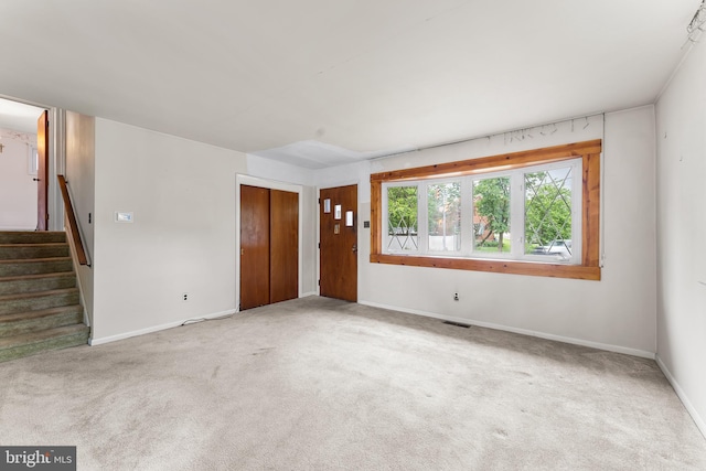 unfurnished living room featuring carpet floors, baseboards, and stairs