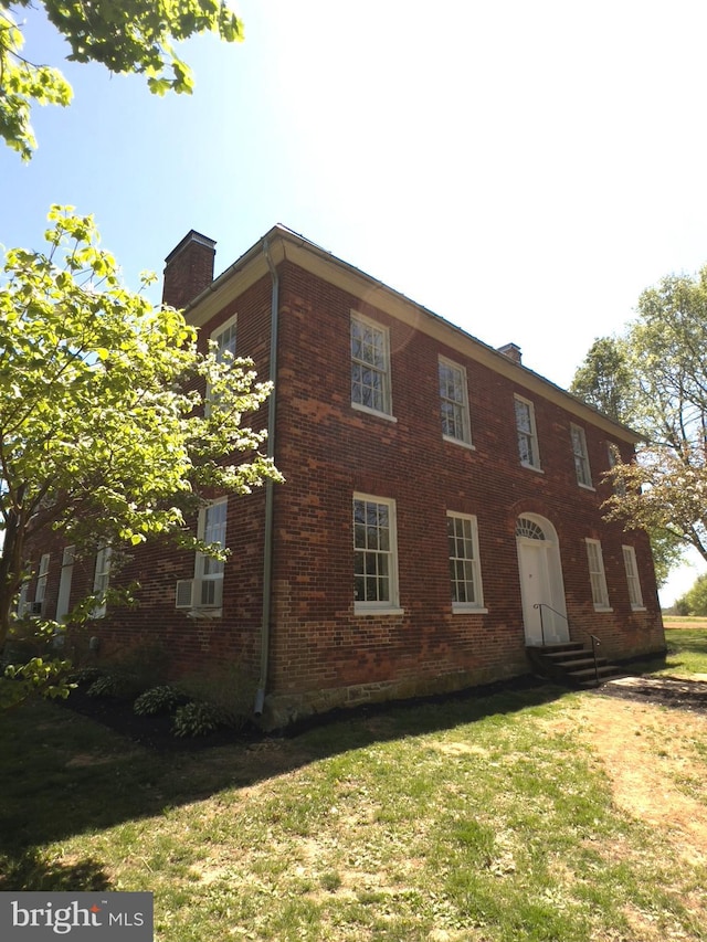view of front of property with a chimney, brick siding, a front lawn, and entry steps